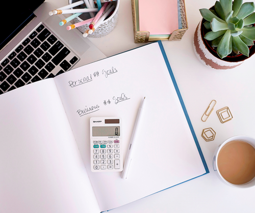 Calculator, coffee, notebook and laptop on female coach's desk.
