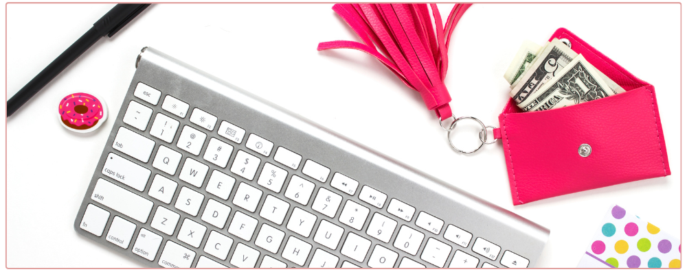 Keyboard with Hot pink wallet and American cash beside it. A pencil, donut eraser and polka dot notpad